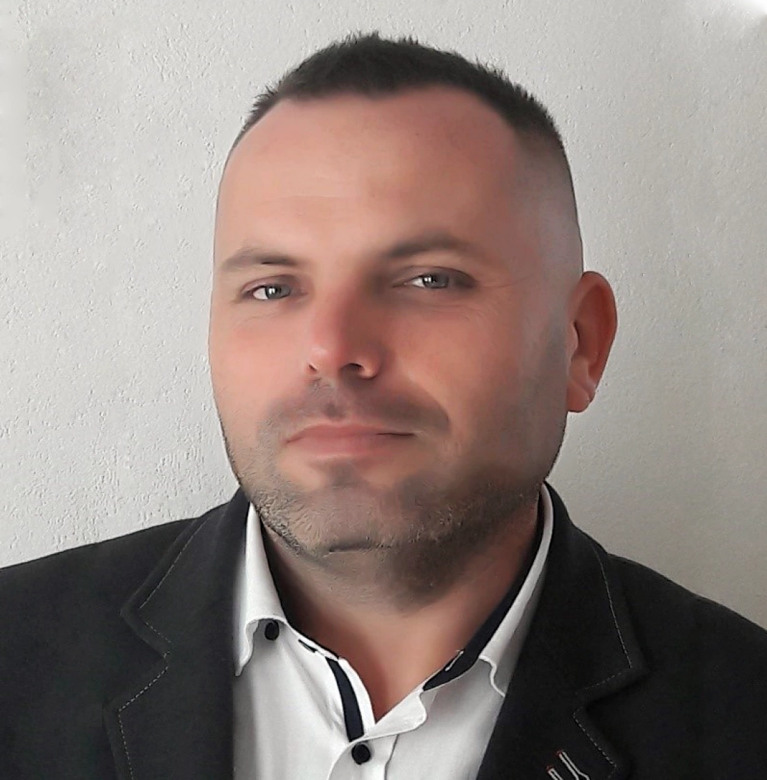 Mężczyzna w eleganckiej marynarce, patrzący w kamerę na neutralnym tle.