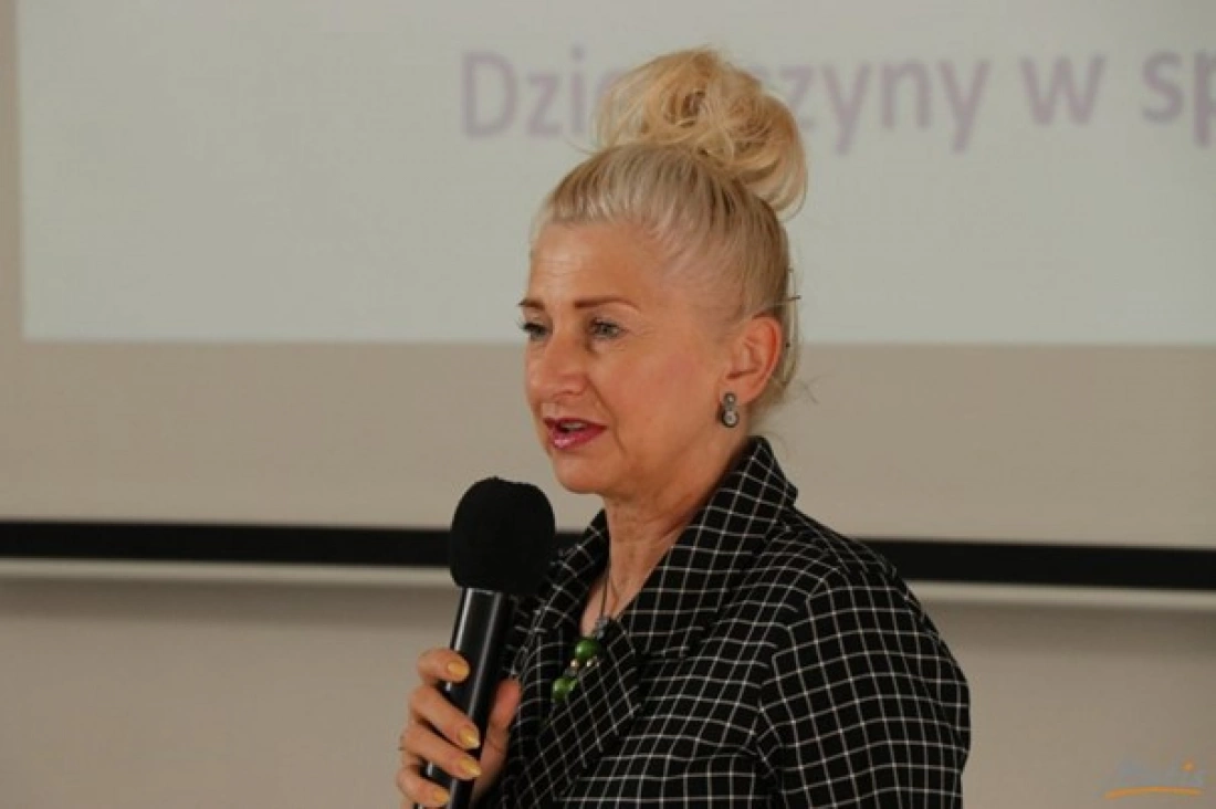 Kobieta z mikrofonem przemawia na tle ekranu.