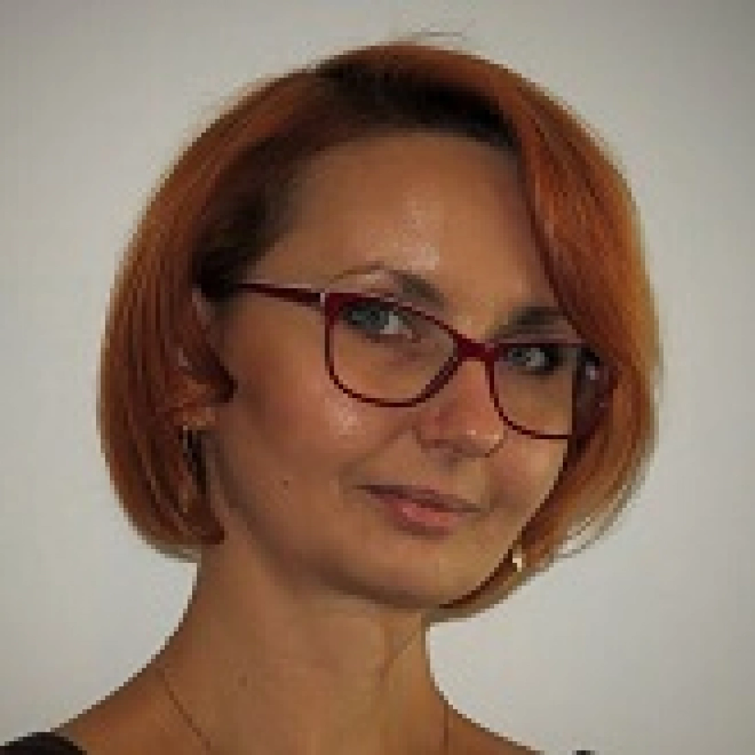 Kobieta z krótkimi, rudymi włosami i okularami, uśmiechająca się lekko.