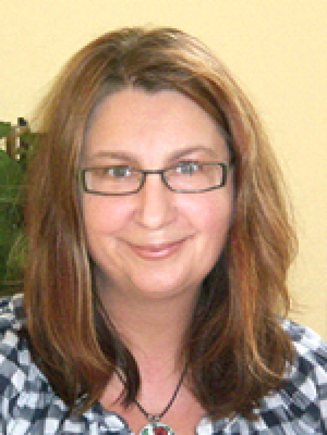 Uśmiechnięta osoba w okularach z długimi włosami, w koszuli w kratę.