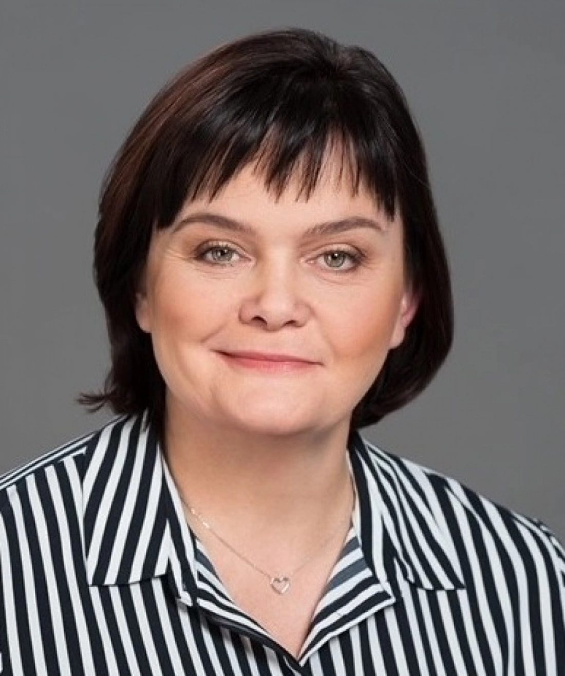 Kobieta z krótkimi czarnymi włosami, uśmiechająca się, w bluzce w paski.