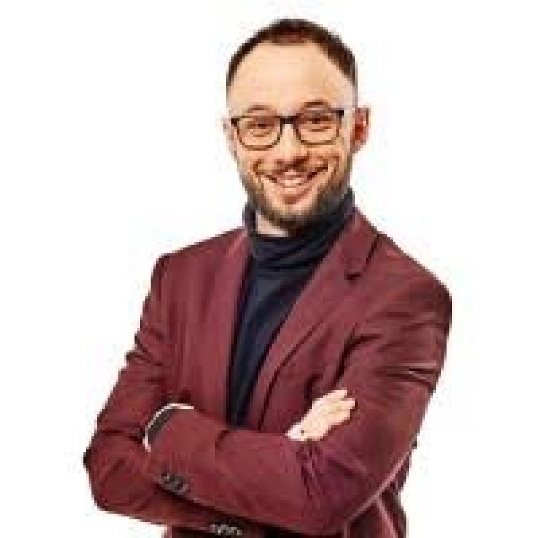 Uśmiechnięty mężczyzna w okularach z założonymi rękami, ubrany w burgundowy żakiet.