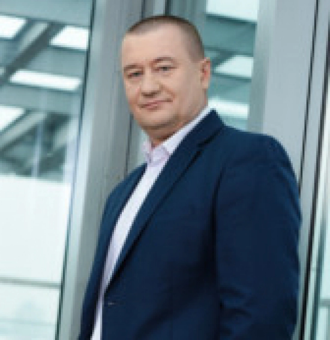 Mężczyzna w garniturze stoi przy dużym oknie w nowoczesnym wnętrzu.