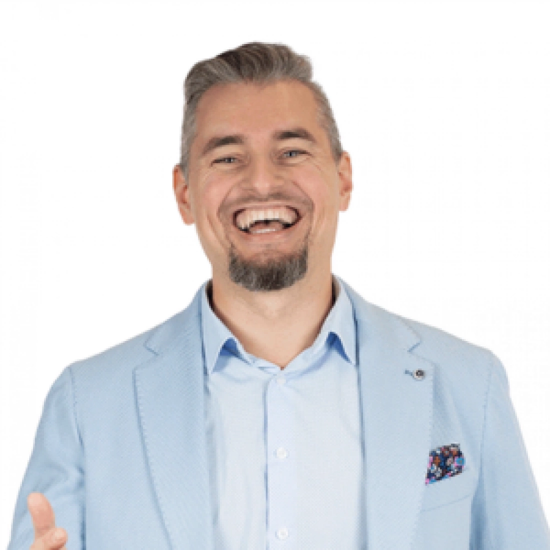 Mężczyzna w jasnym garniturze z uśmiechem, stojący w stylowym wnętrzu.