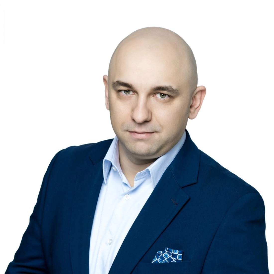 Mężczyzna w eleganckim garniturze, z gładko ogoloną głową, patrzy prosto w obiektyw.