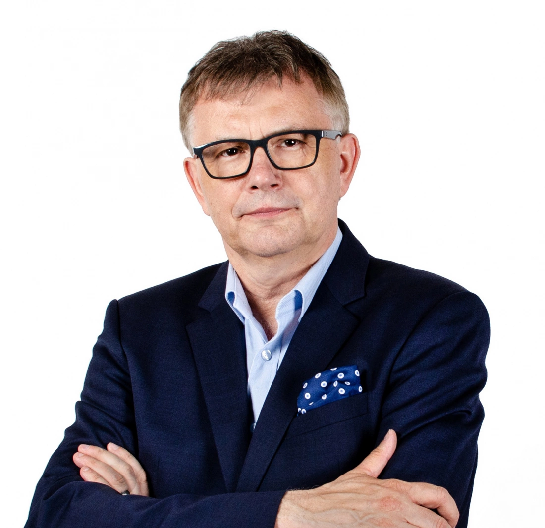 Mężczyzna w garniturze z założonymi rękami, na tle białym.
