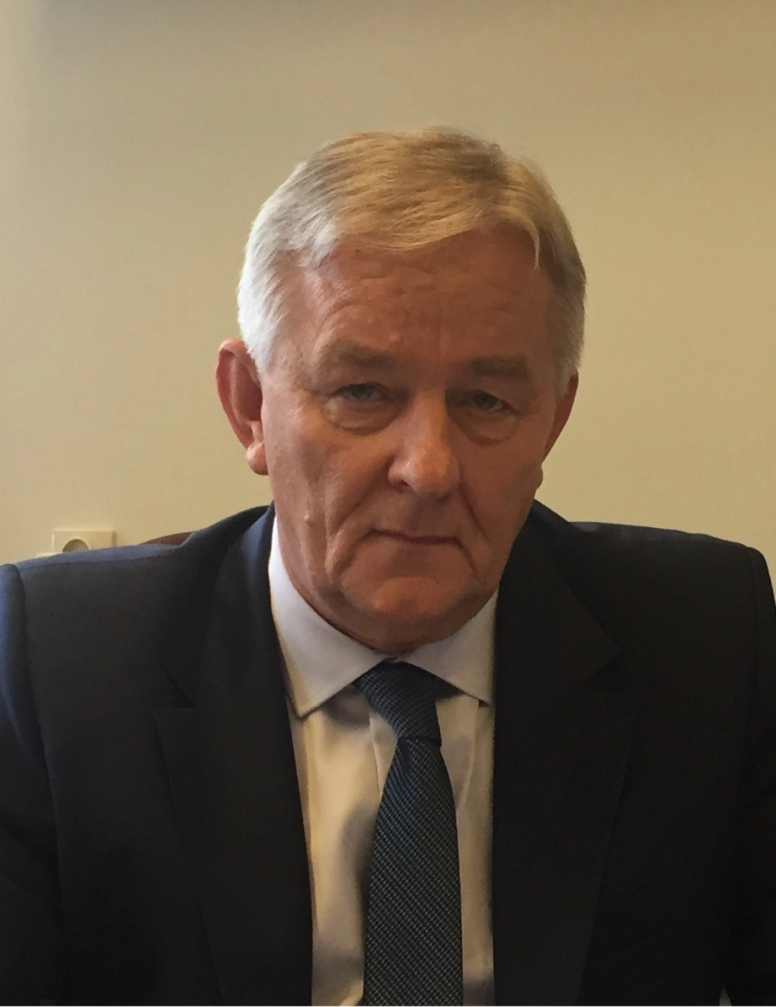 Mężczyzna w garniturze siedzi z poważnym wyrazem twarzy.