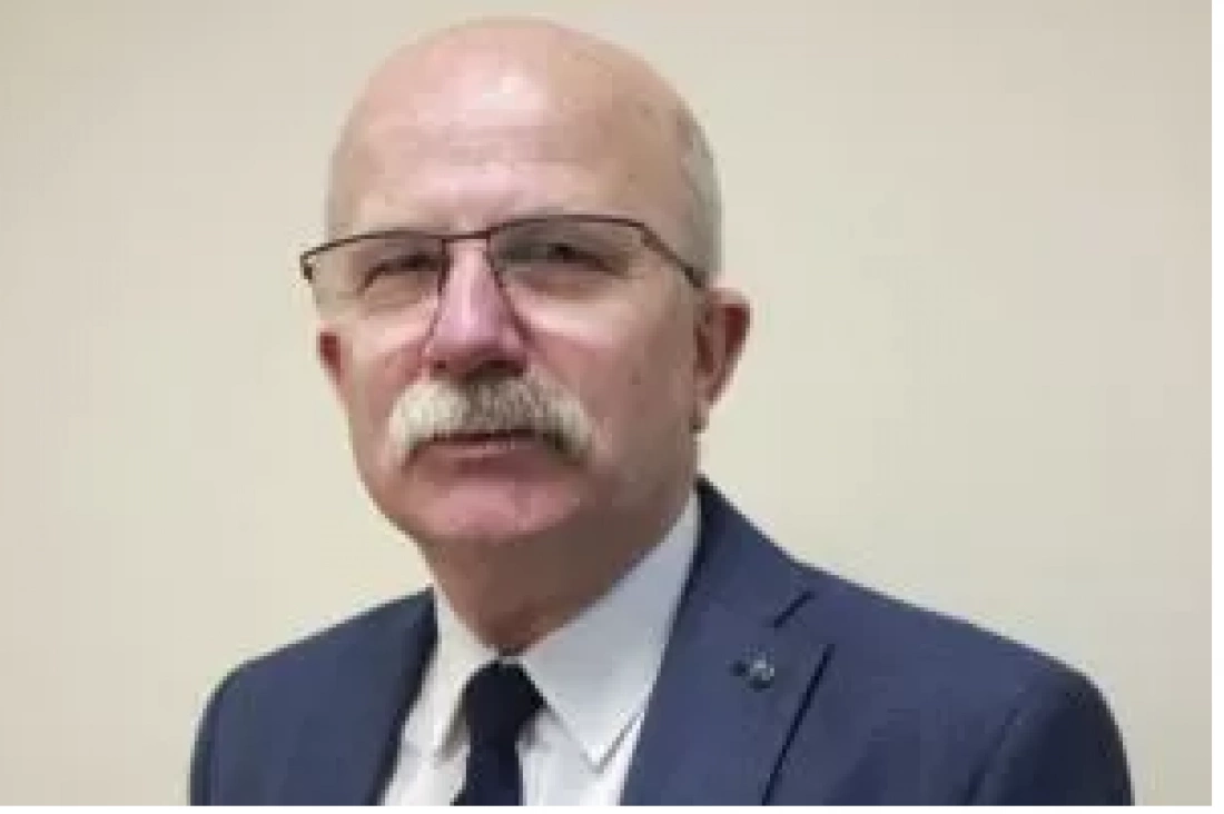 Mężczyzna w okularach, z siwymi wąsami, ubrany w garnitur.