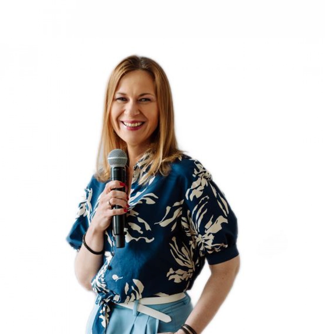 Kobieta w kwiecistej bluzce trzyma mikrofon, uśmiechając się do kamery.