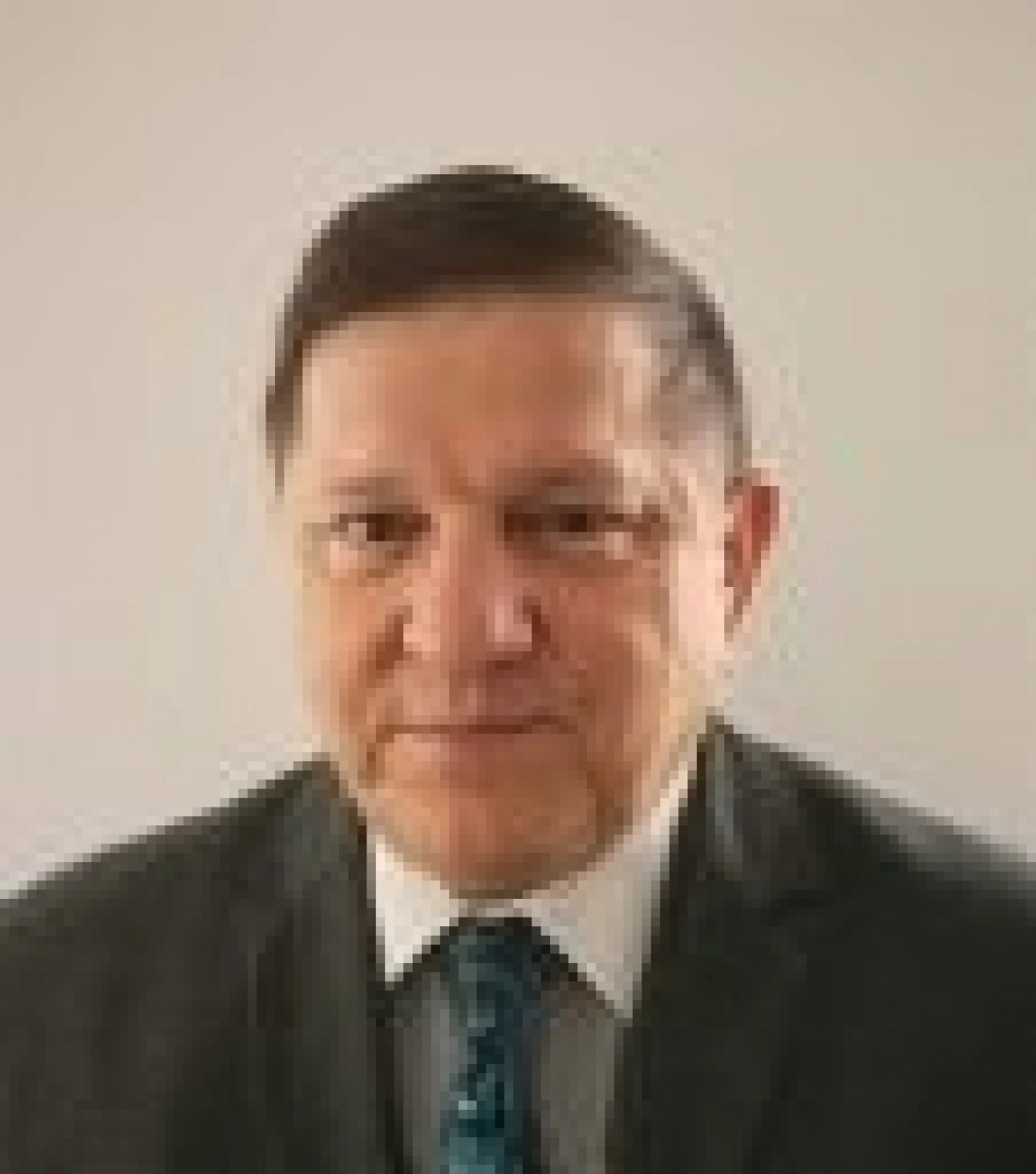 Mężczyzna w garniturze z krawatem, patrzący w kamerę. Tło jasne.