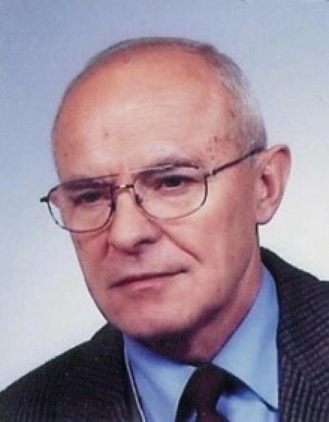 Mężczyzna w okularach, w garniturze, z poważnym wyrazem twarzy.