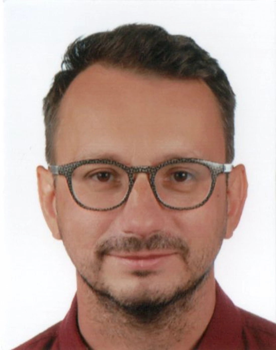 Mężczyzna z okularami i ciemnymi włosami, uśmiechający się do kamery.