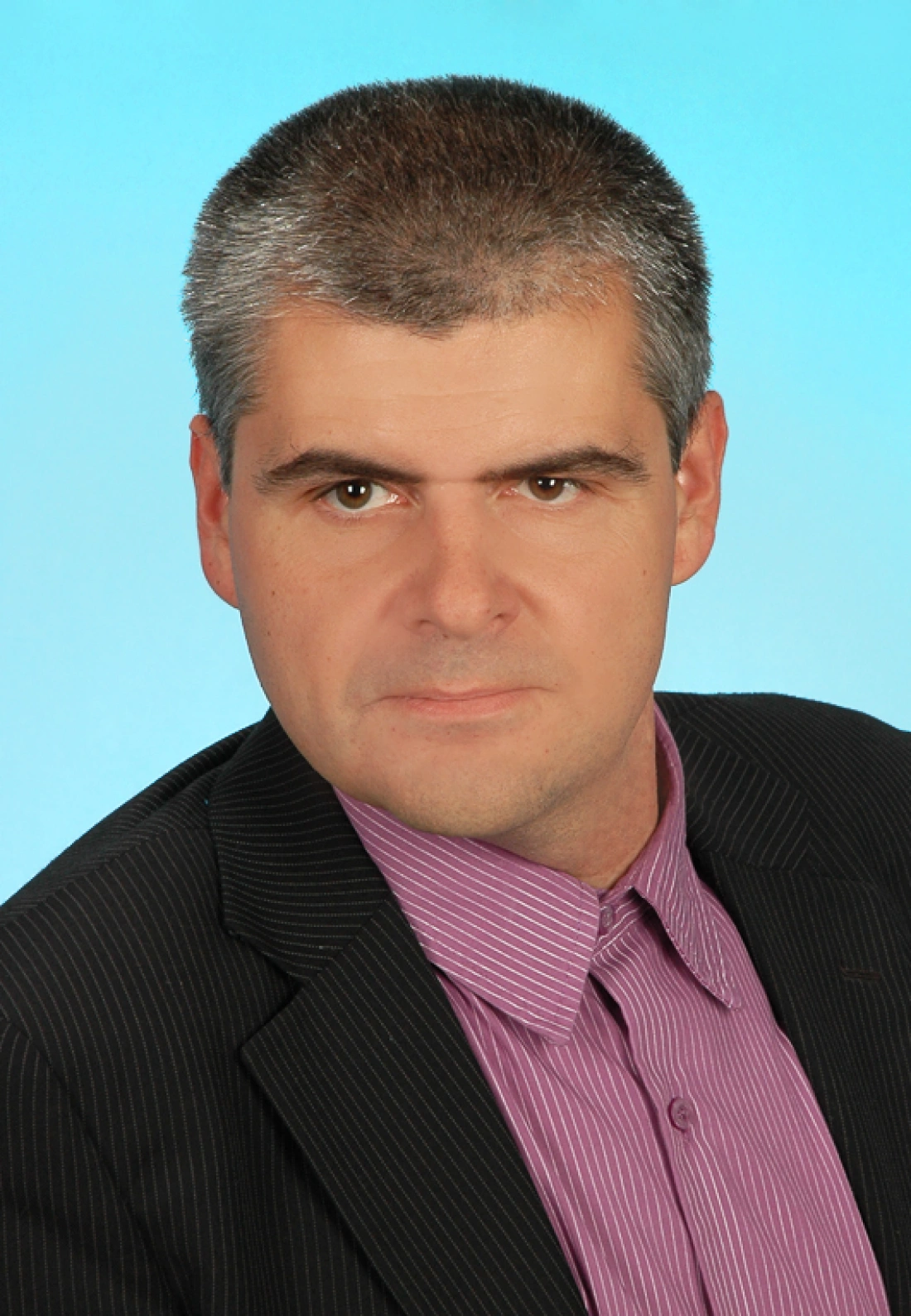 Mężczyzna w stylowym garniturze z krótkimi włosami na tle niebieskiej ściany.