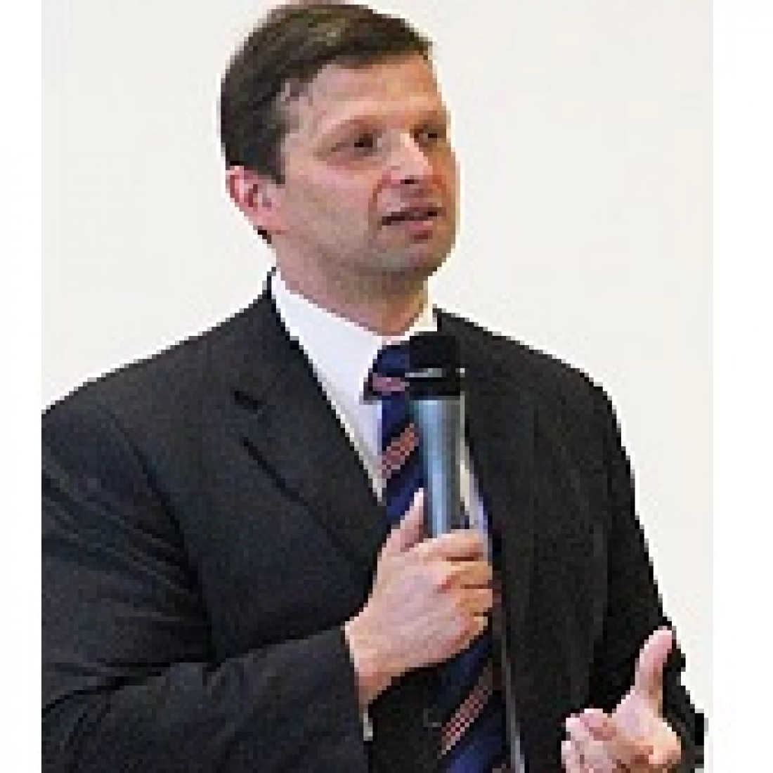 Mężczyzna w garniturze trzyma mikrofon i wygłasza przemówienie.