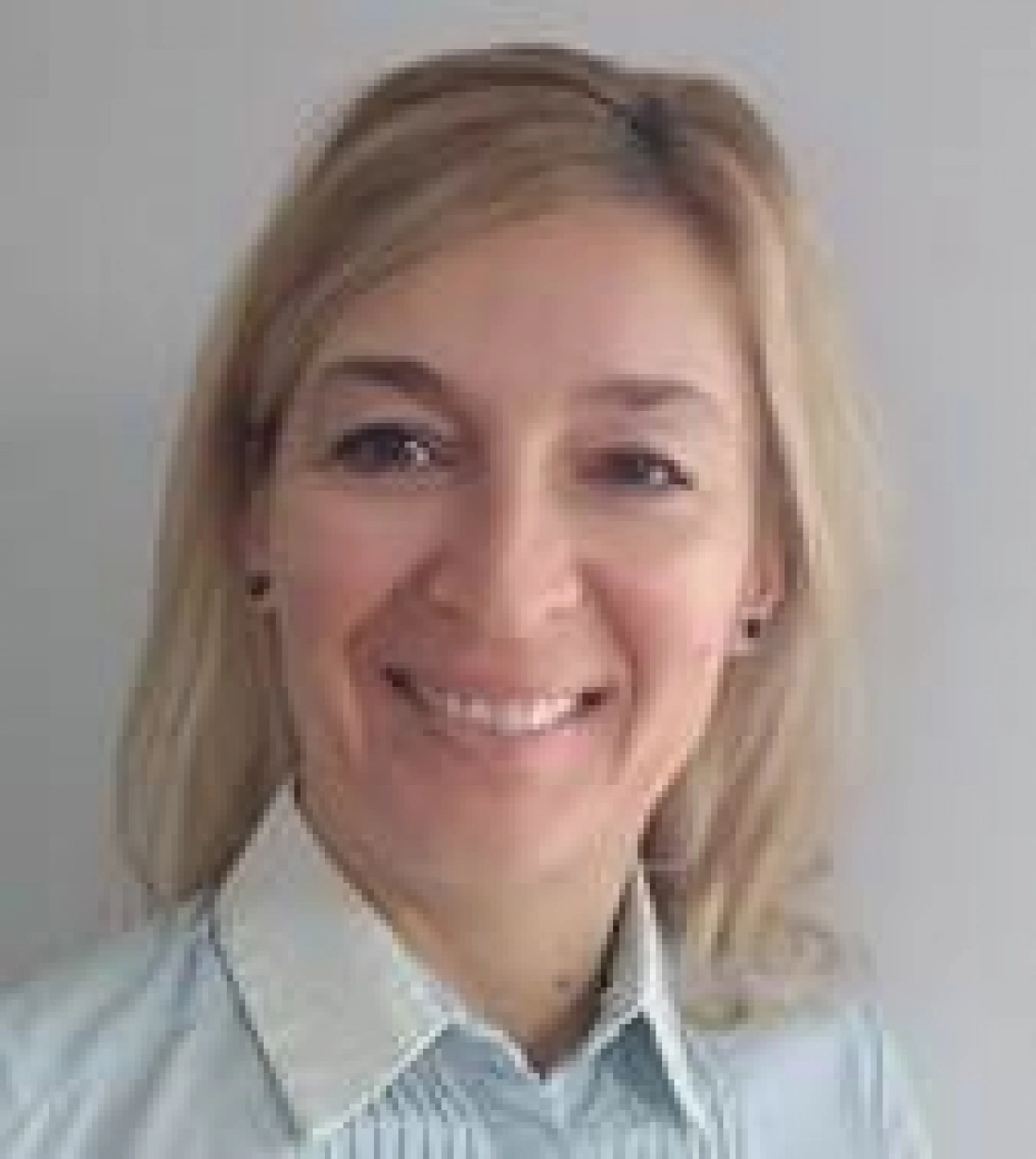 Kobieta z blond włosami, uśmiechnięta, w jasnej koszuli.