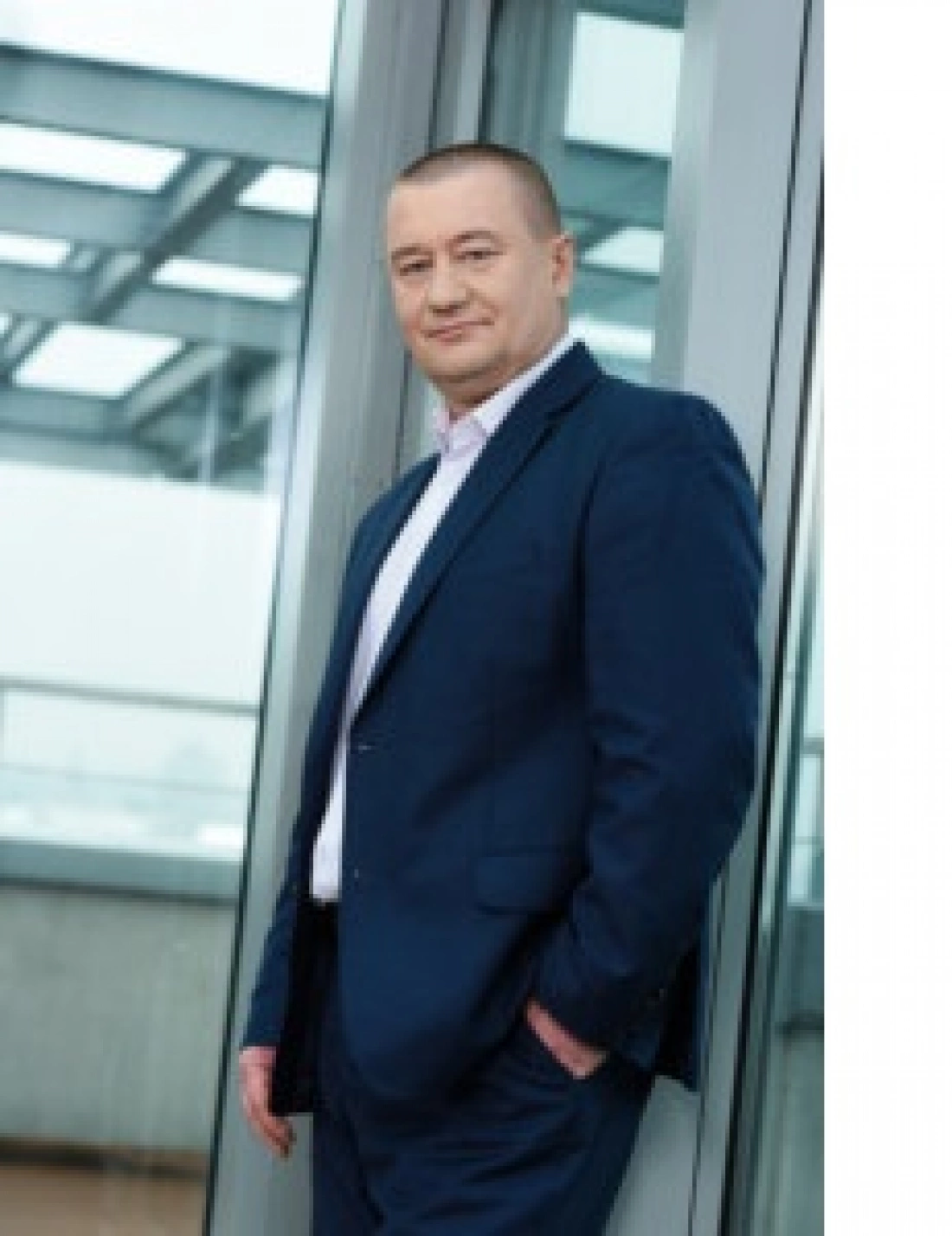 Mężczyzna w granatowym garniturze stoi obok szklanej ściany.