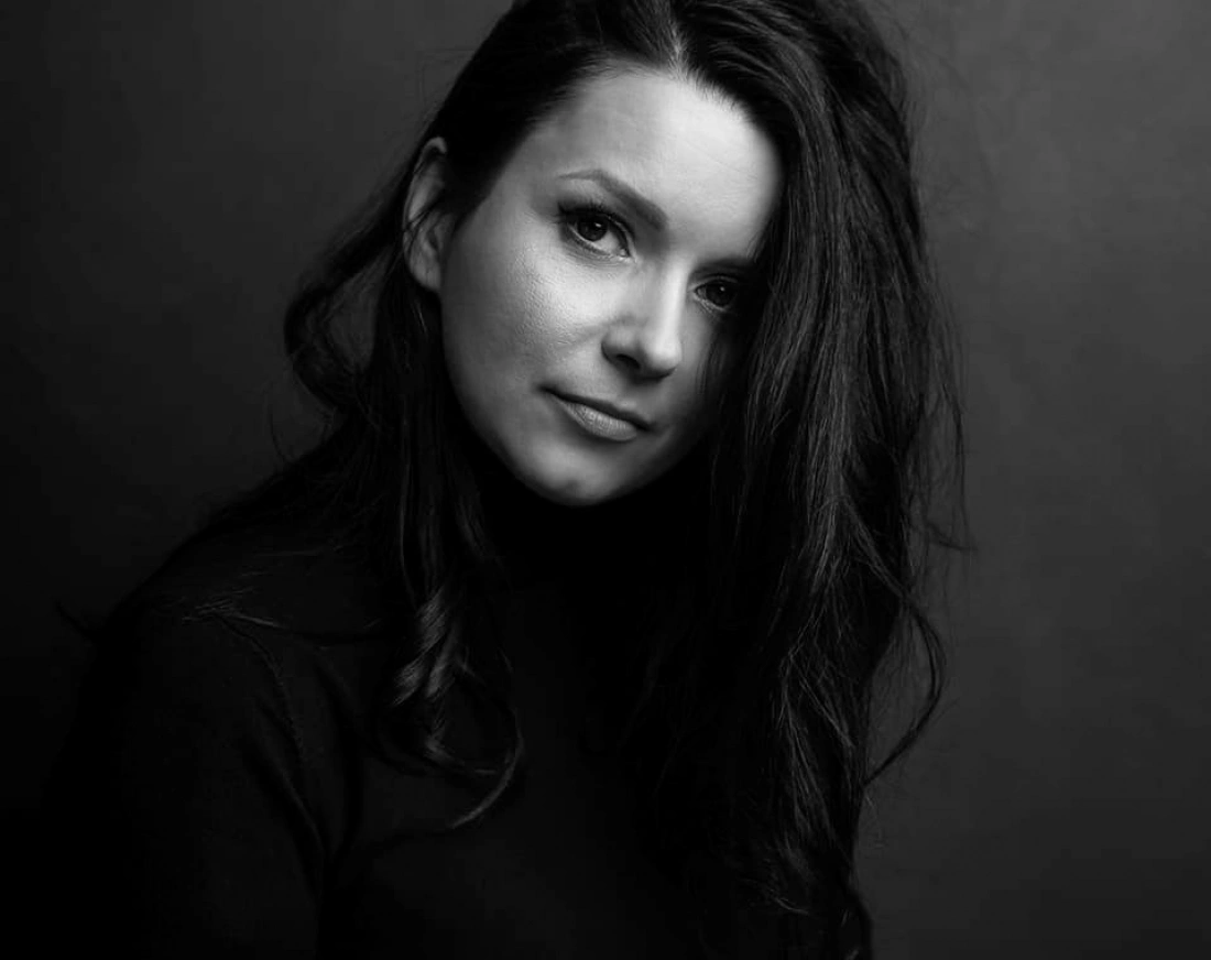 Czarno-biała fotografia kobiety z długimi, ciemnymi włosami, patrzącej w stronę obiektywu.