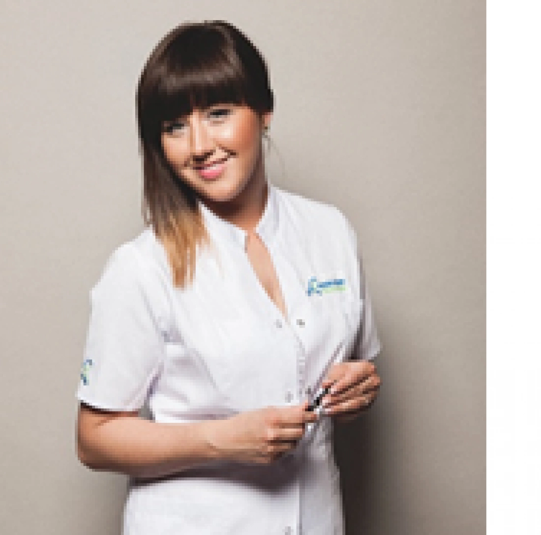 Młoda kobieta w białym mundurze, trzymająca długopis, uśmiecha się do zdjęcia.