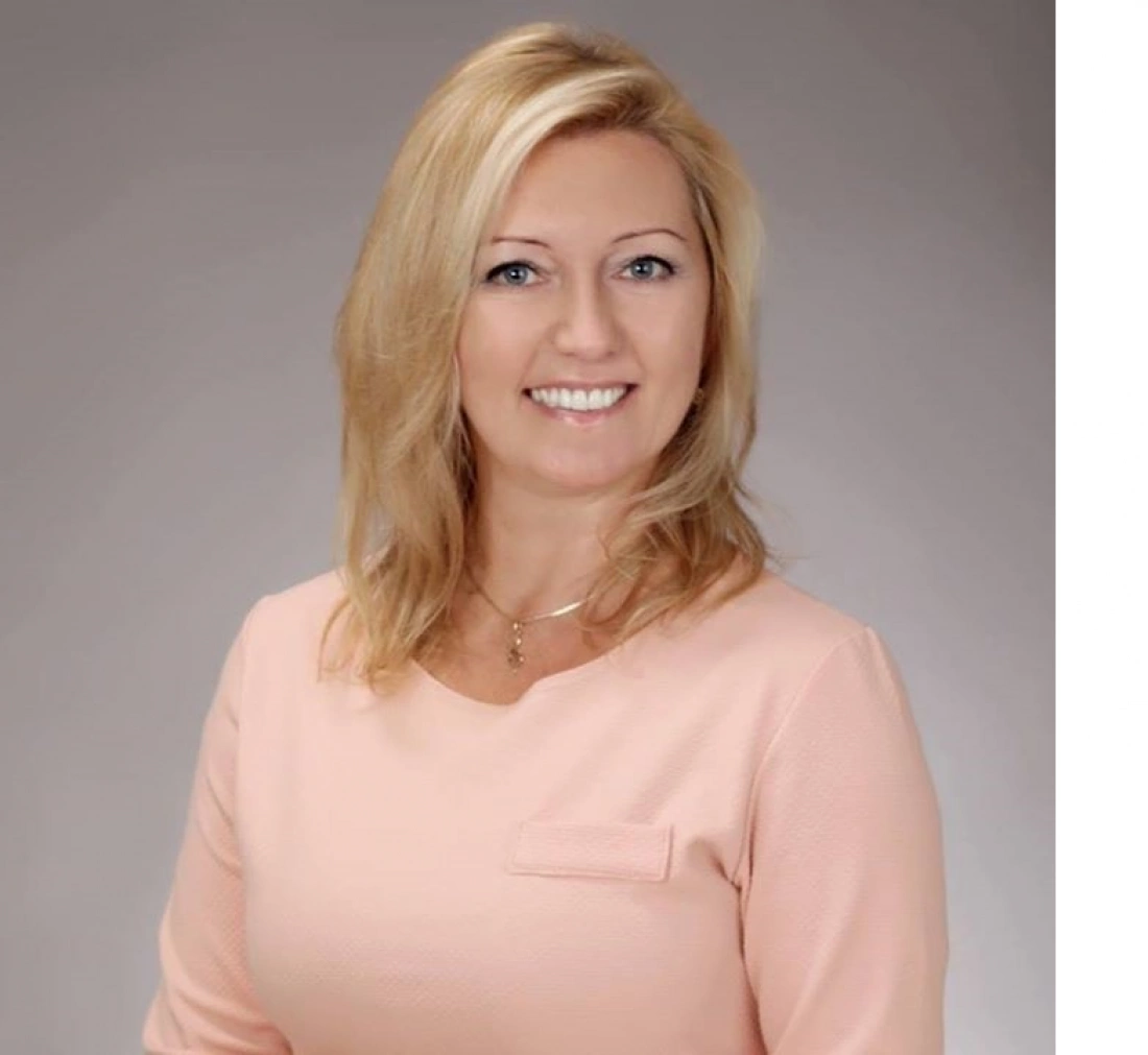 Kobieta o blond włosach, uśmiechająca się, ubrana w różową bluzkę.