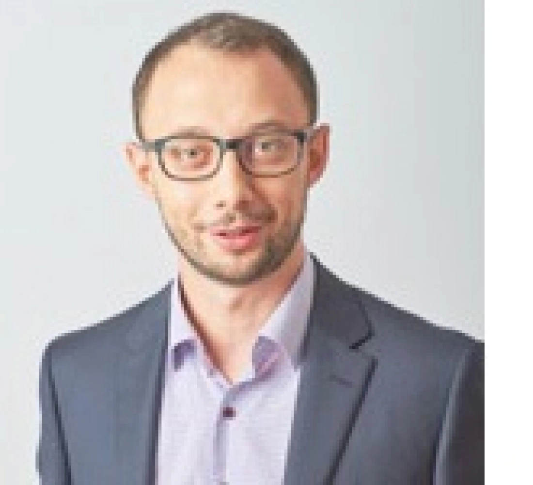 Mężczyzna w okularach, w garniturze, uśmiechający się do aparatu.