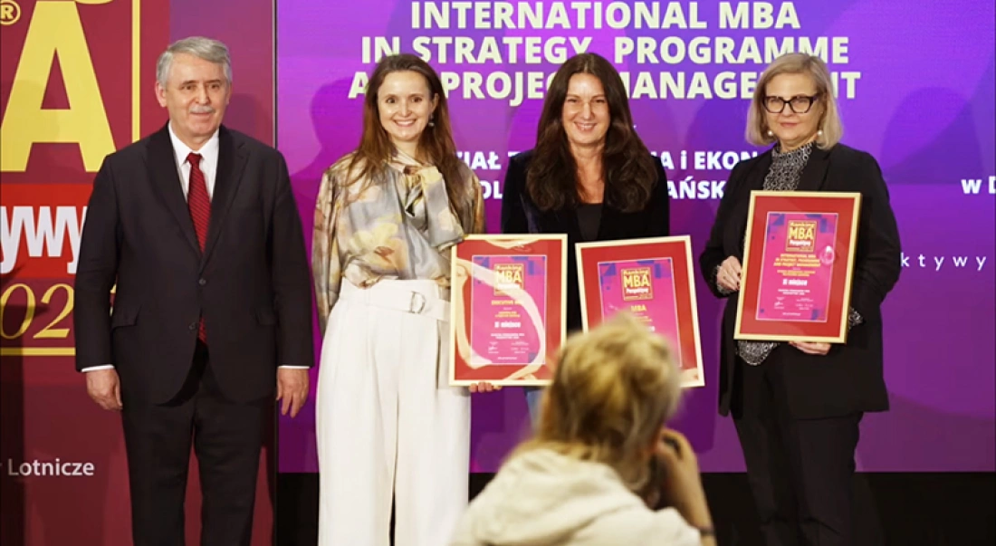 Cztery osoby stoją na tle kolorowego znaku "Ranking MBA 2023", trzymając dyplomy.