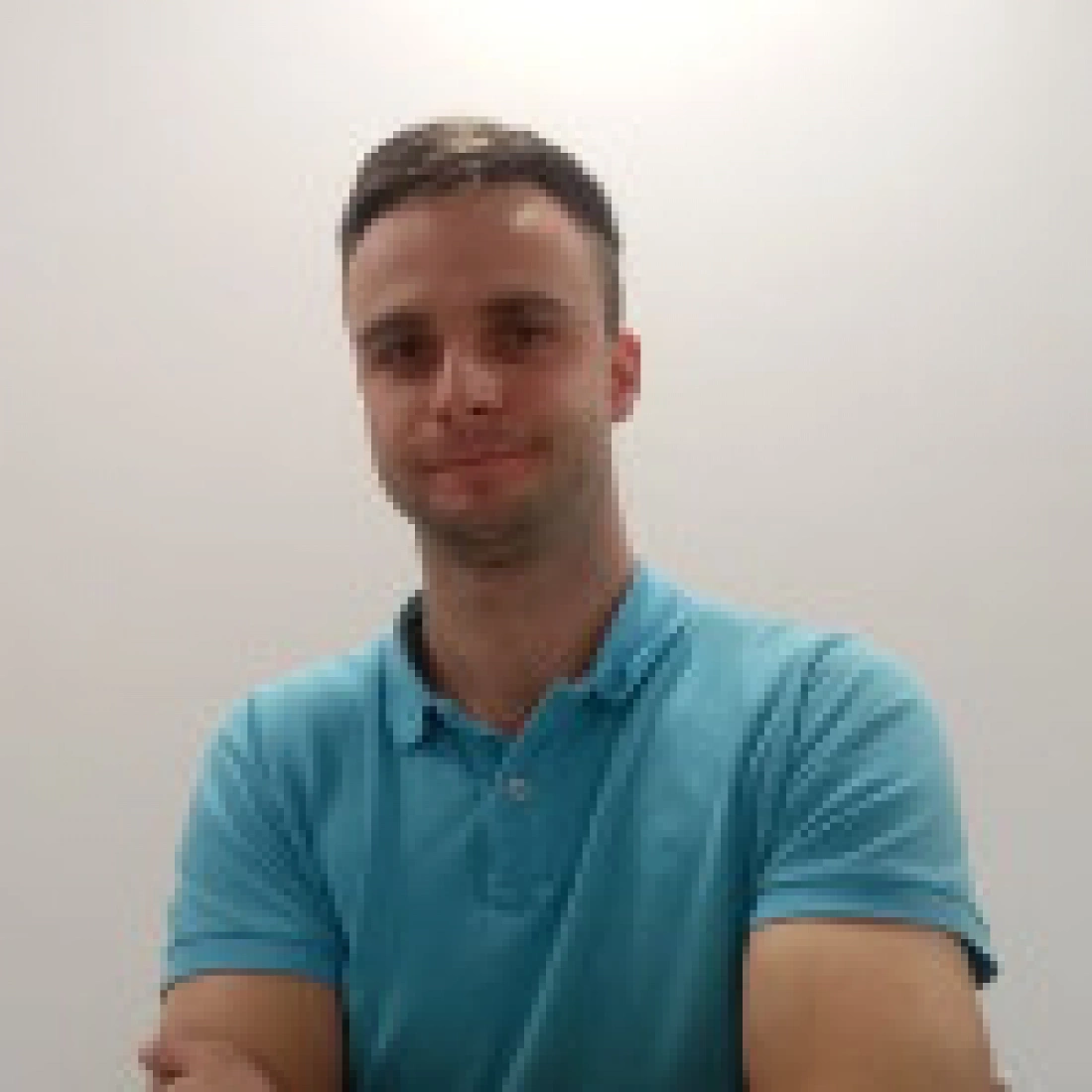 Mężczyzna w niebieskiej koszulce polo, uśmiechający się z założonymi rękoma.