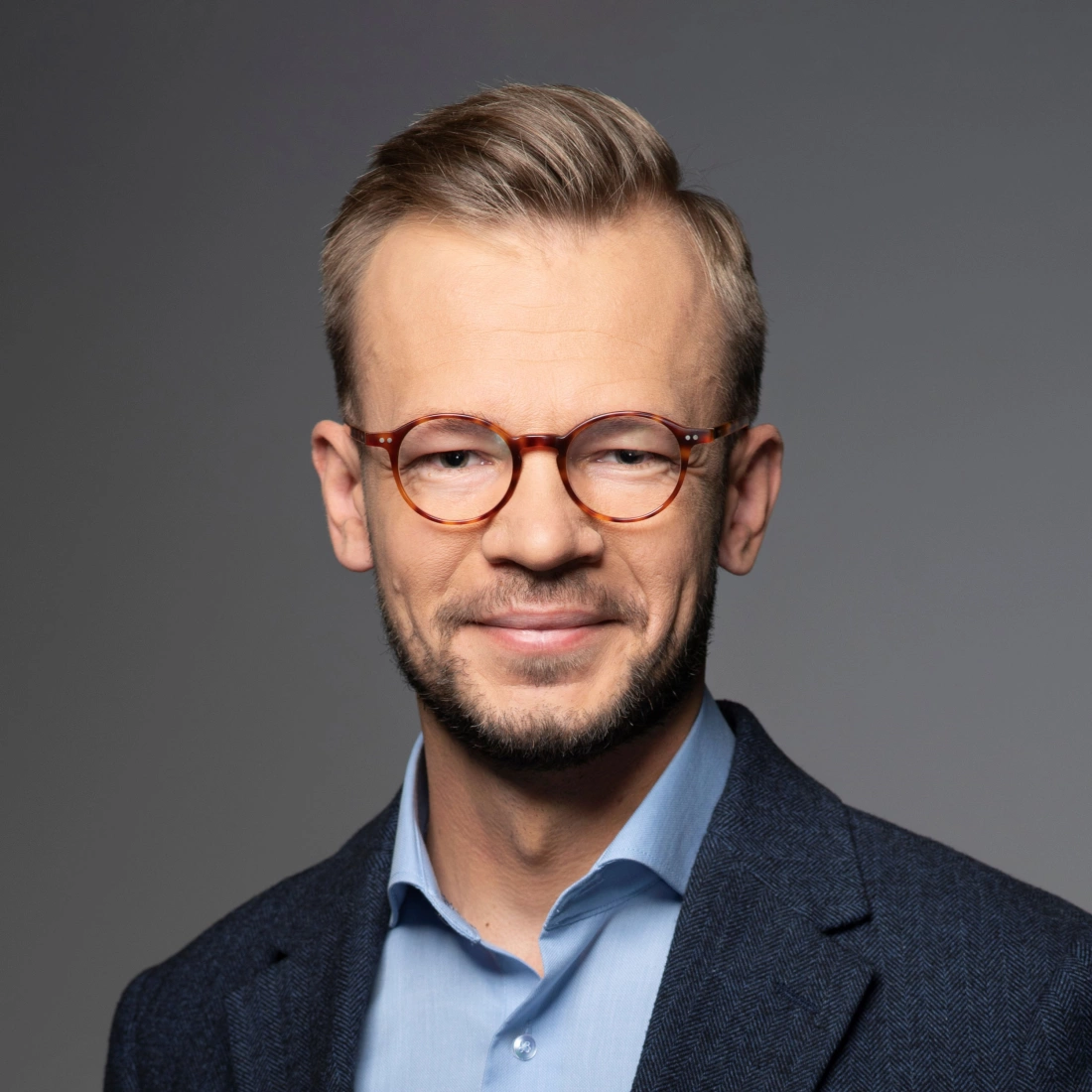 Mężczyzna w okularach, uśmiechający się na tle w jednolitym kolorze.