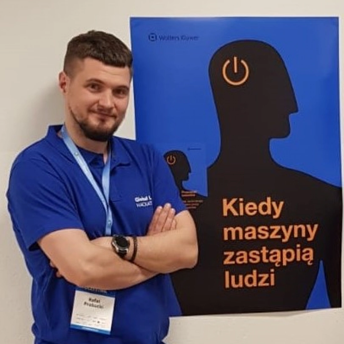 Mężczyzna w niebieskiej koszuli stoi obok plakatu z napisem "Kiedy maszyny zastąpią ludzi".