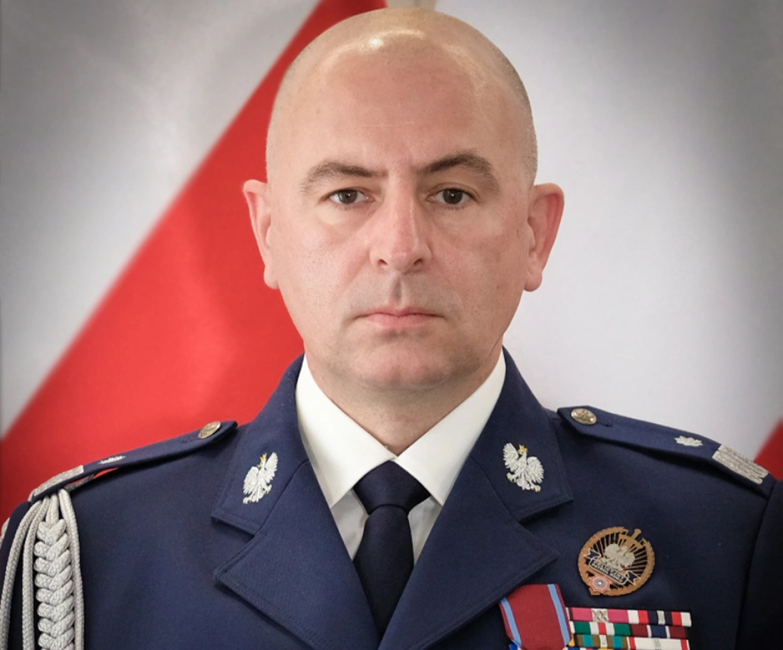 Mężczyzna w mundurze wojskowym, z medalami i odznaczeniami, na tle flagi.