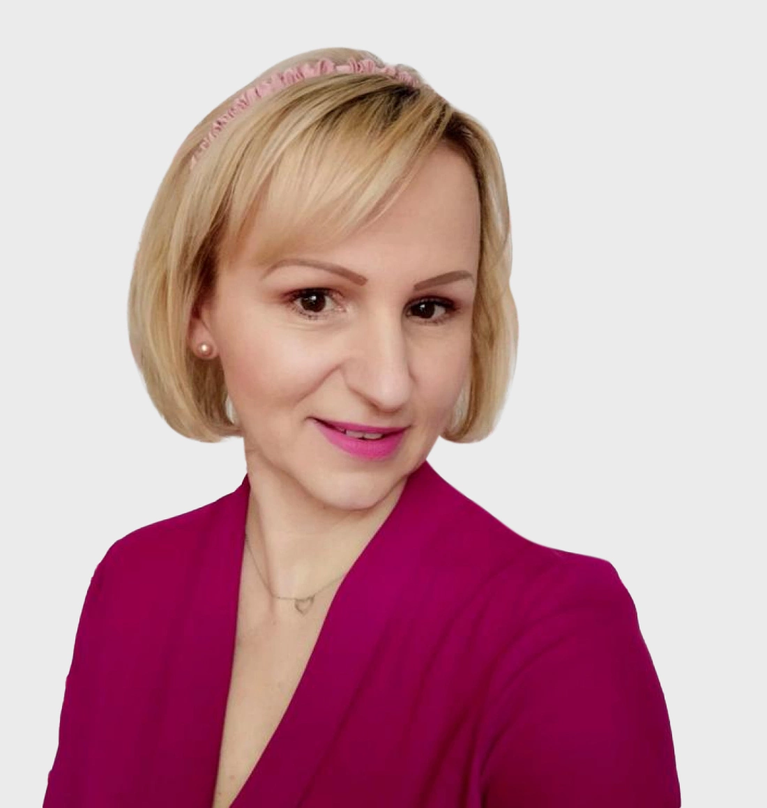 Kobieta z krótkimi blond włosami, w różowej bluzce, z uśmiechem i delikatnym makijażem.