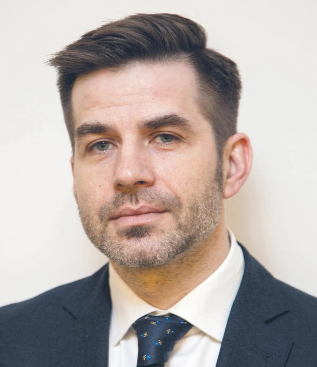 Mężczyzna w garniturze z brodą, patrzący prosto w obiektyw.