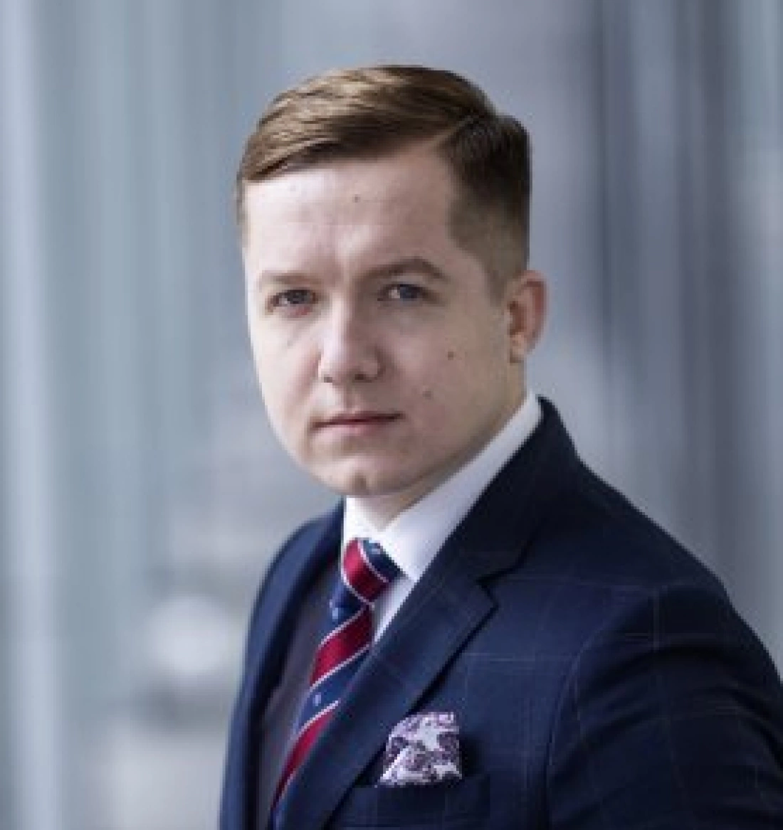 Formalny portret mężczyzny w garniturze, z krótkimi włosami i zdecydowanym wyrazem twarzy.