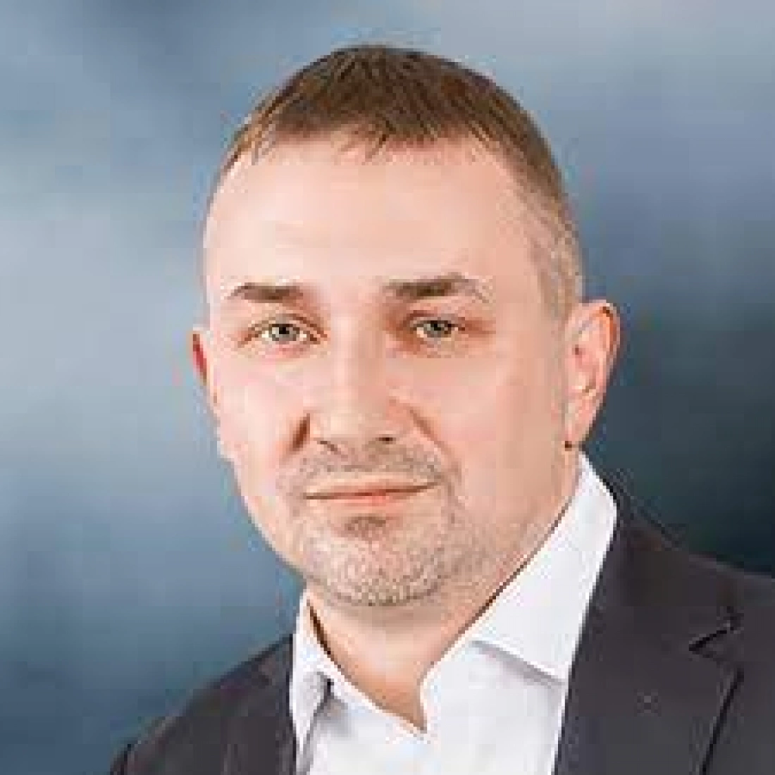 Mężczyzna w eleganckim garniturze, z krótkimi włosami i wyrazistym spojrzeniem.