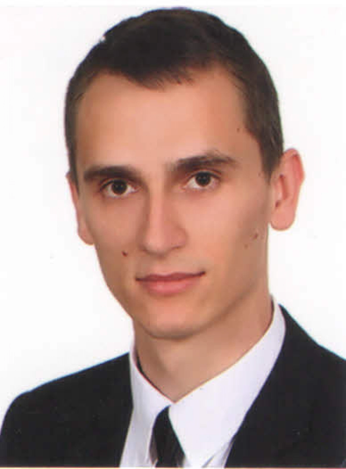 Mężczyzna w formalnym ubiorze, z krótkimi włosami i neutralnym wyrazem twarzy.
