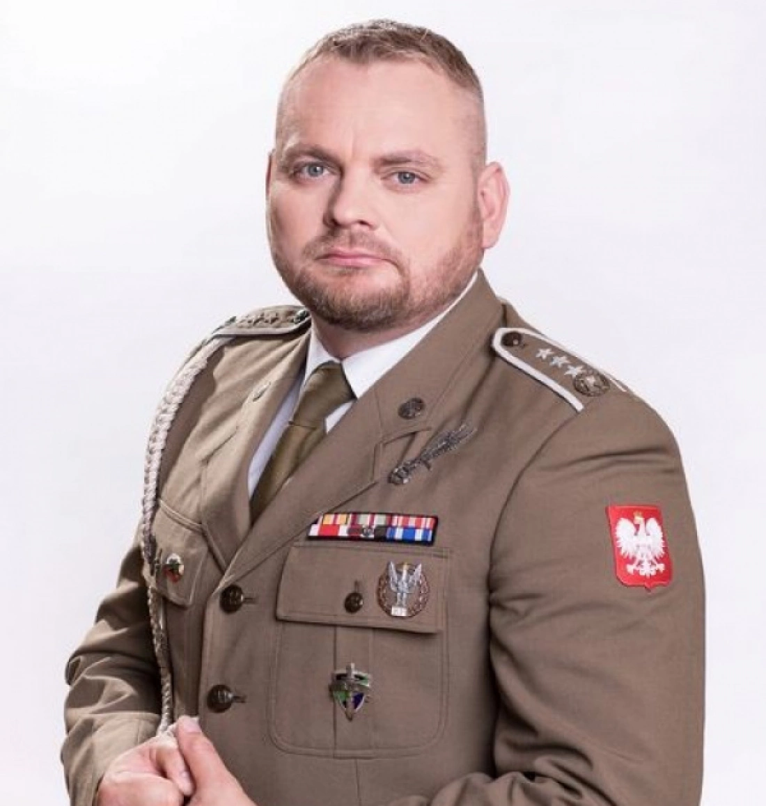 Mężczyzna w mundurze wojskowym z odznaczeniami, pozujący na tle białego tła.