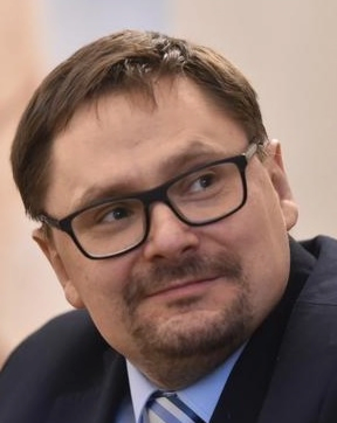 Mężczyzna z okularami, uśmiechający się i występujący w garniturze.