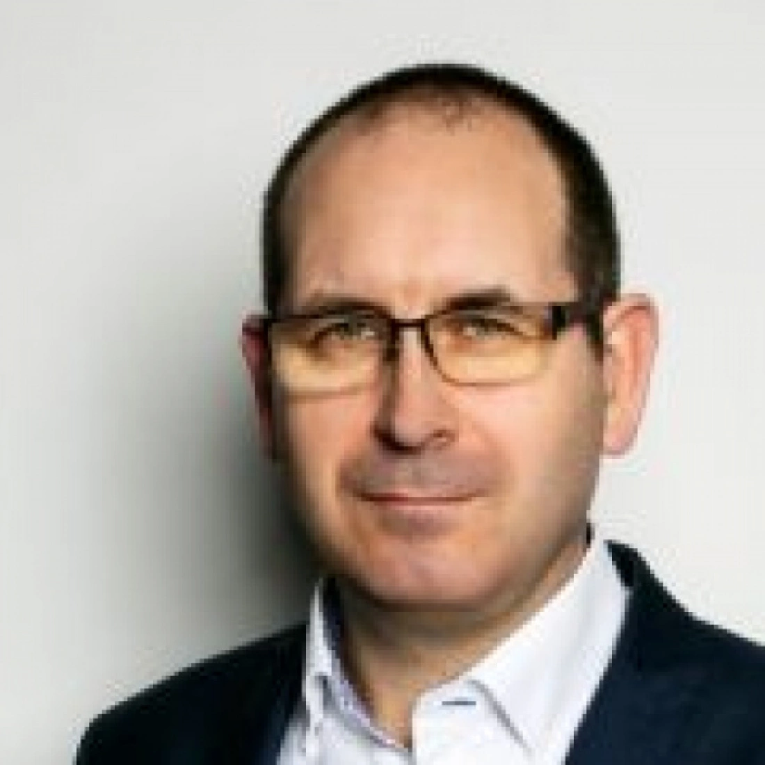 Mężczyzna w okularach, uśmiechający się na neutralnym tle.