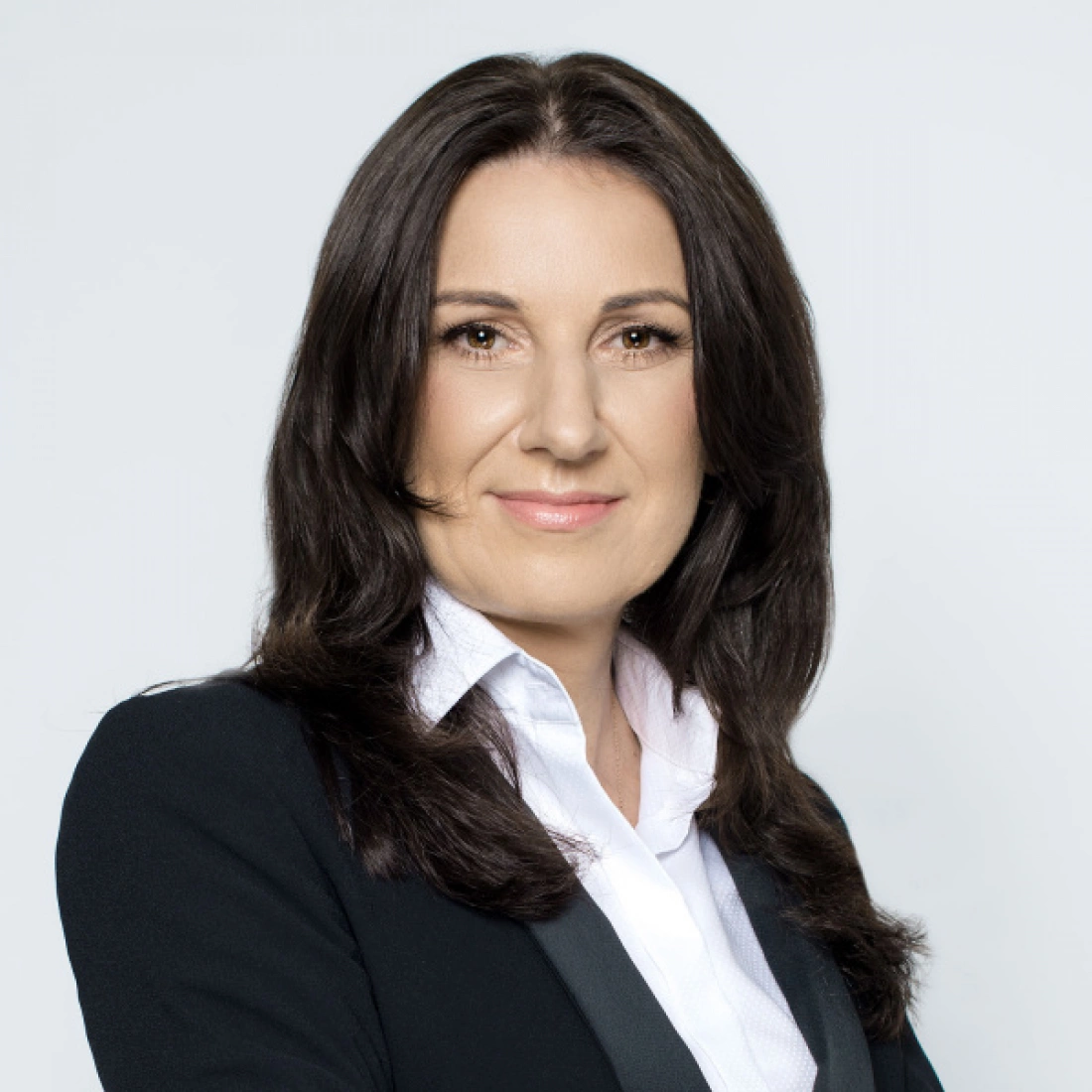 Kobieta w eleganckim stroju, uśmiechająca się, na tle jasnego tła.