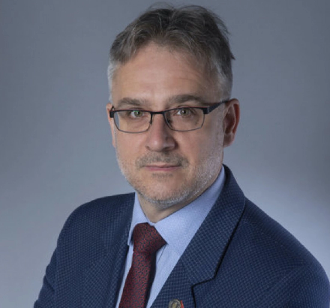 Mężczyzna w okularach, w garniturze, z poważnym wyrazem twarzy.