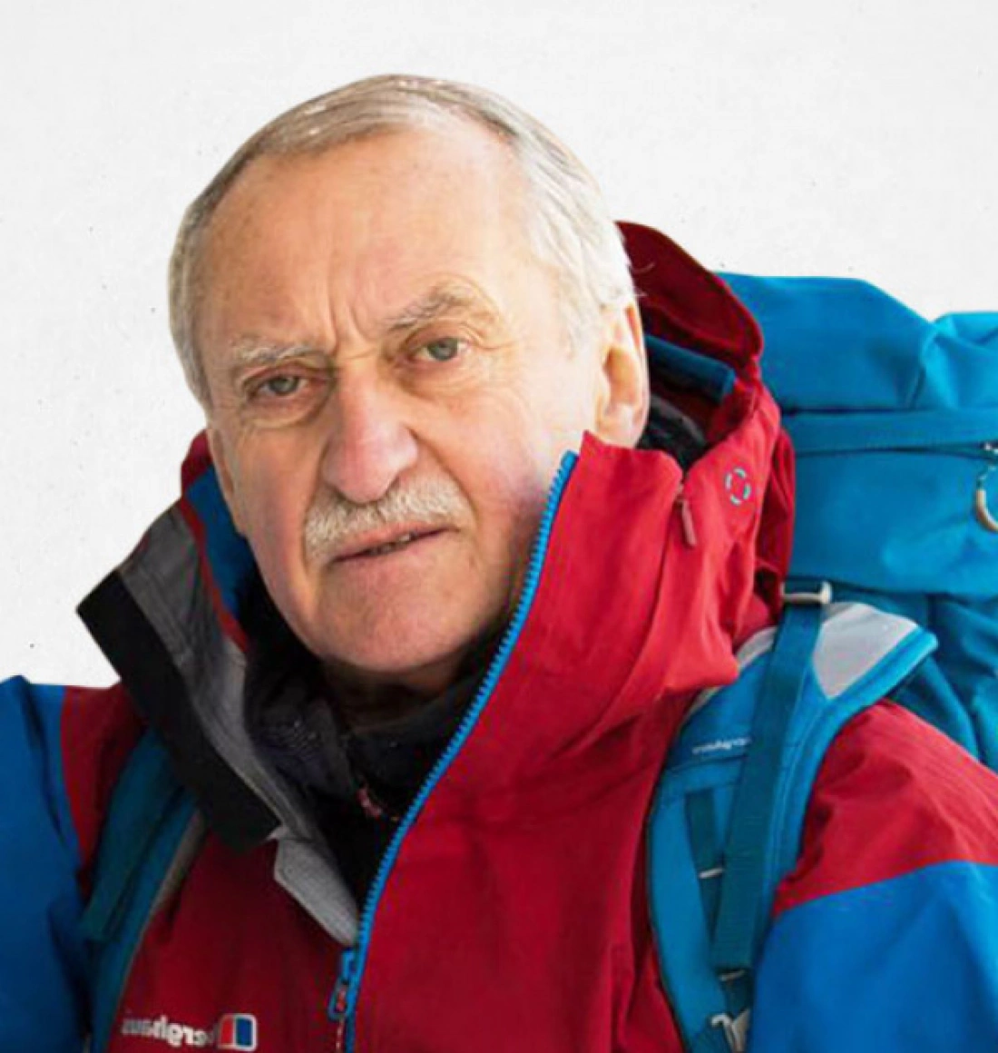 Mężczyzna w czerwonej kurtce turystycznej z niebieskim plecakiem.