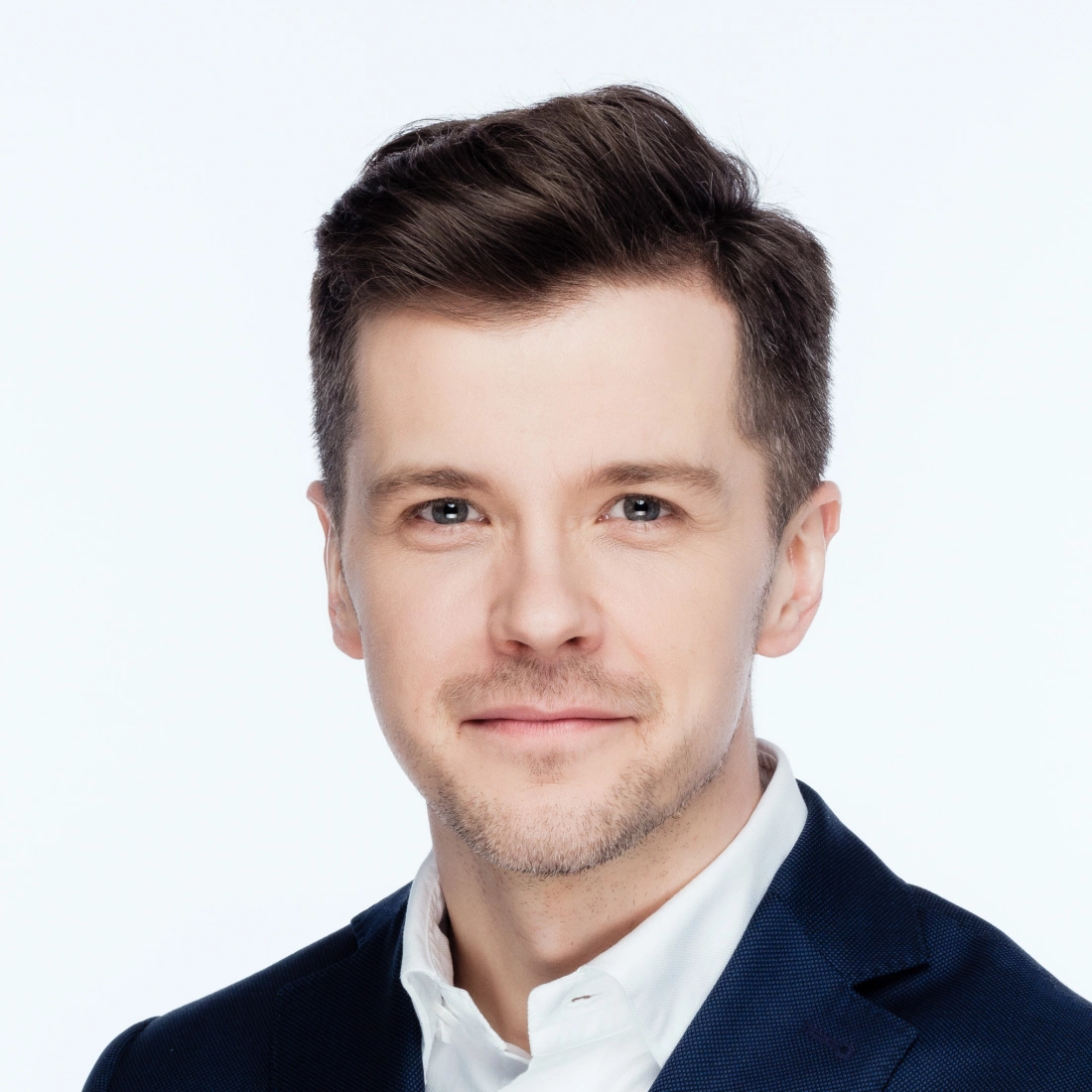 Mężczyzna w eleganckim garniturze, uśmiechający się na jasnym tle.