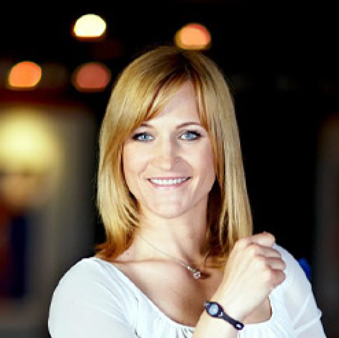 Uśmiechnięta kobieta w białej bluzce, z ręką uniesioną w geście pewności siebie.