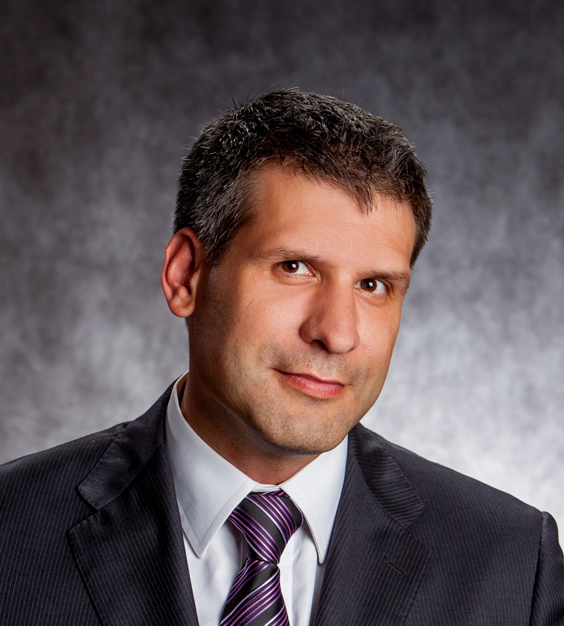 Mężczyzna w eleganckim garniturze z krawatem, uśmiechający się do kamery.