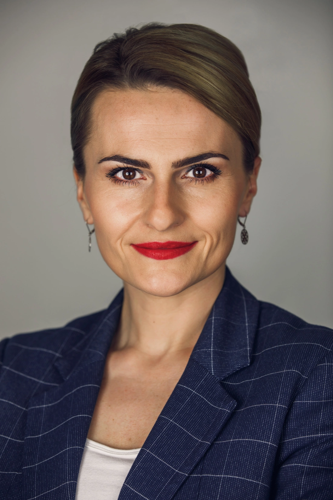 Portret kobiety w eleganckim ubraniu z zamkniętymi ustami i uśmiechem.