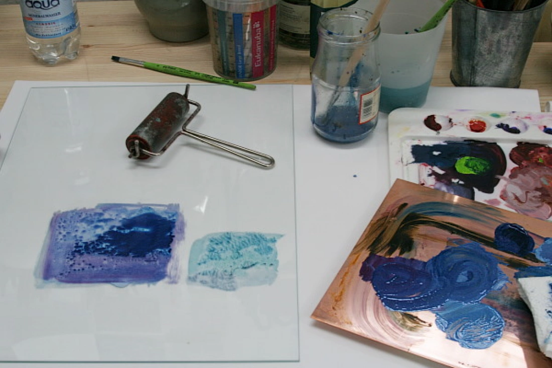 Stół artystyczny z farbami, wałkiem malarskim i paletą kolorów.