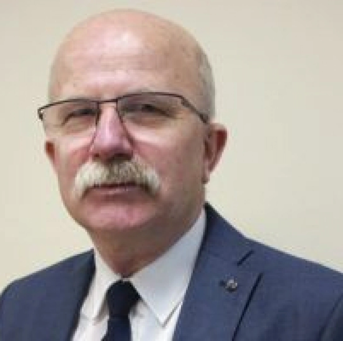 Mężczyzna w okularach, z brodą i w garniturze.