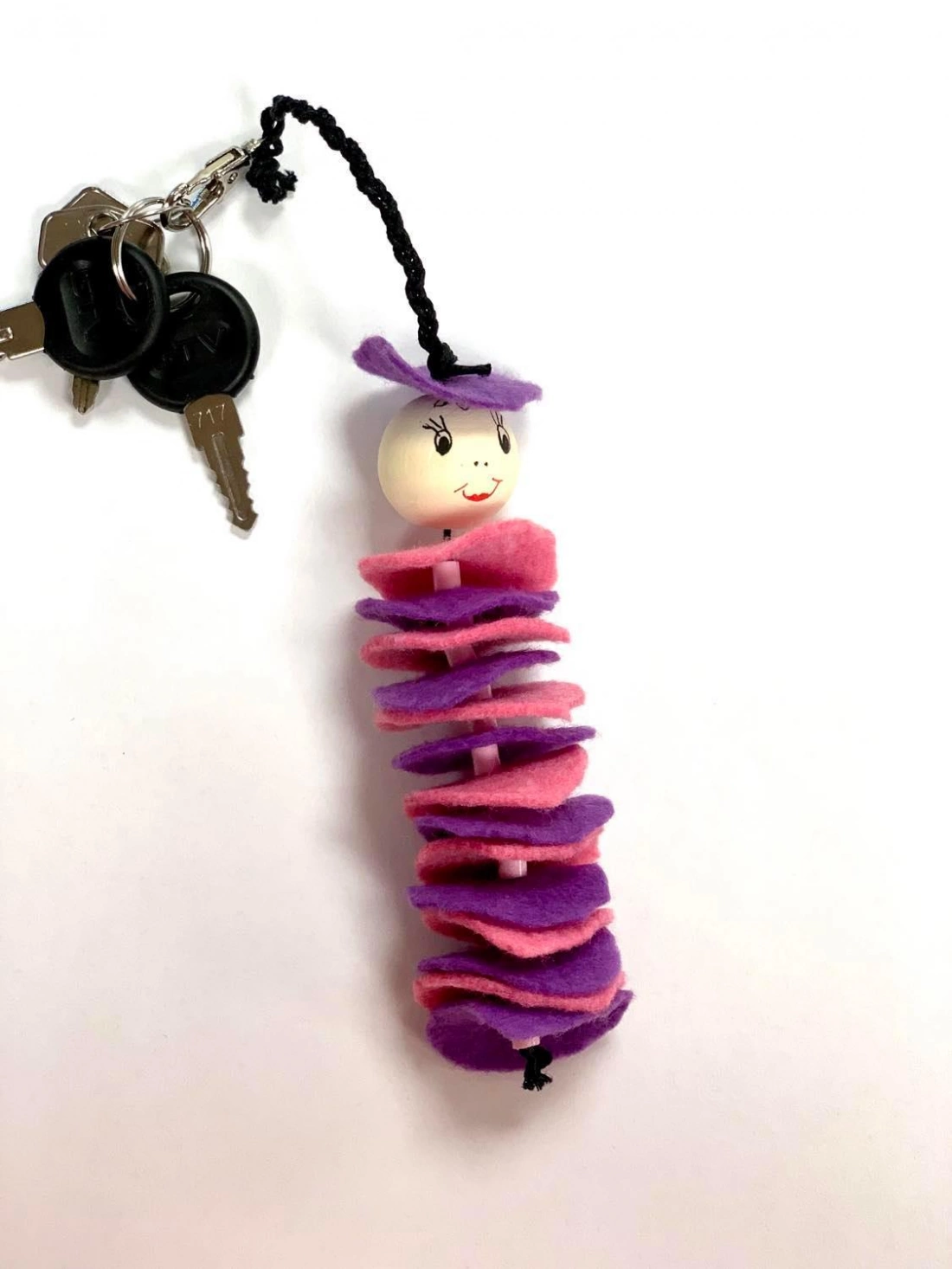 Kolorowy breloczek w kształcie kukiełki, z filcowym ciałem w odcieniach różu i fioletu.
