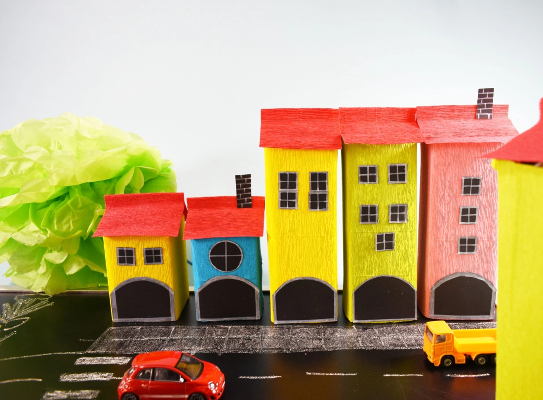 Zestaw kolorowych domków z papieru w miniaturek na tle ulicy i samochodów.