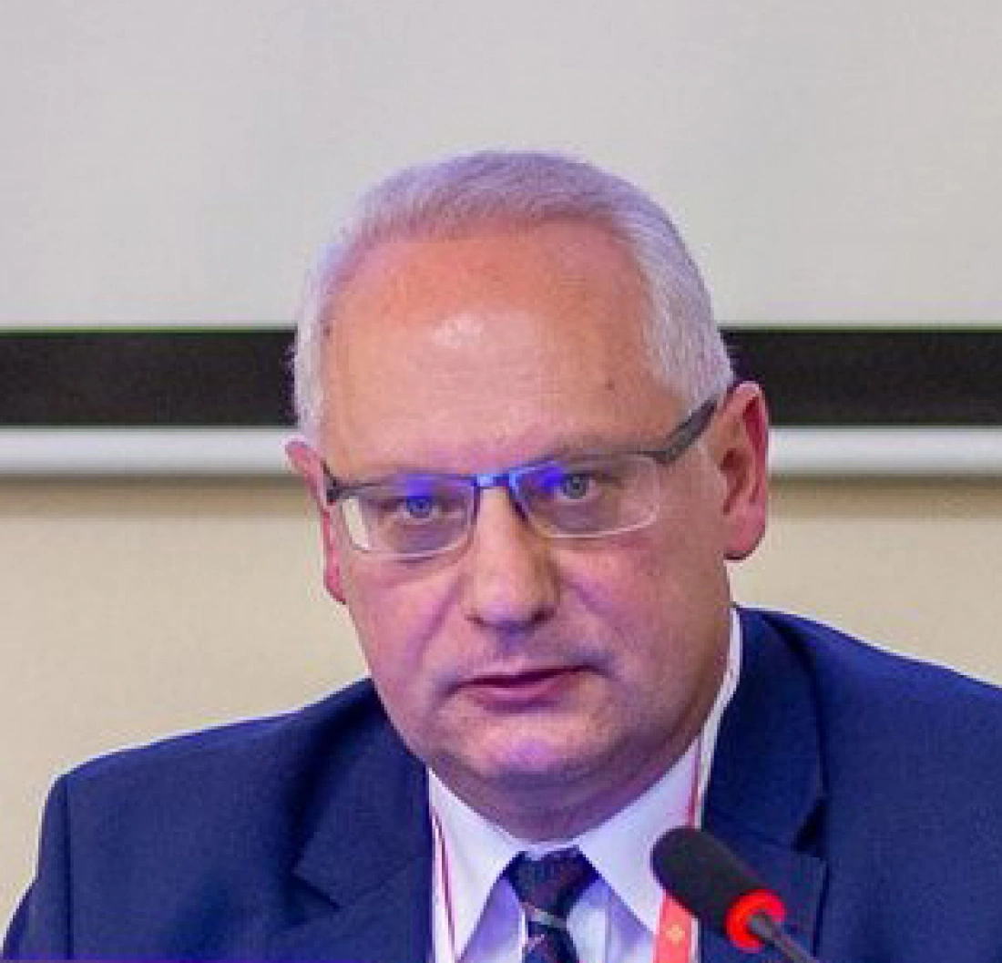 Mężczyzna w okularach, w garniturze, siedzący przy stole.