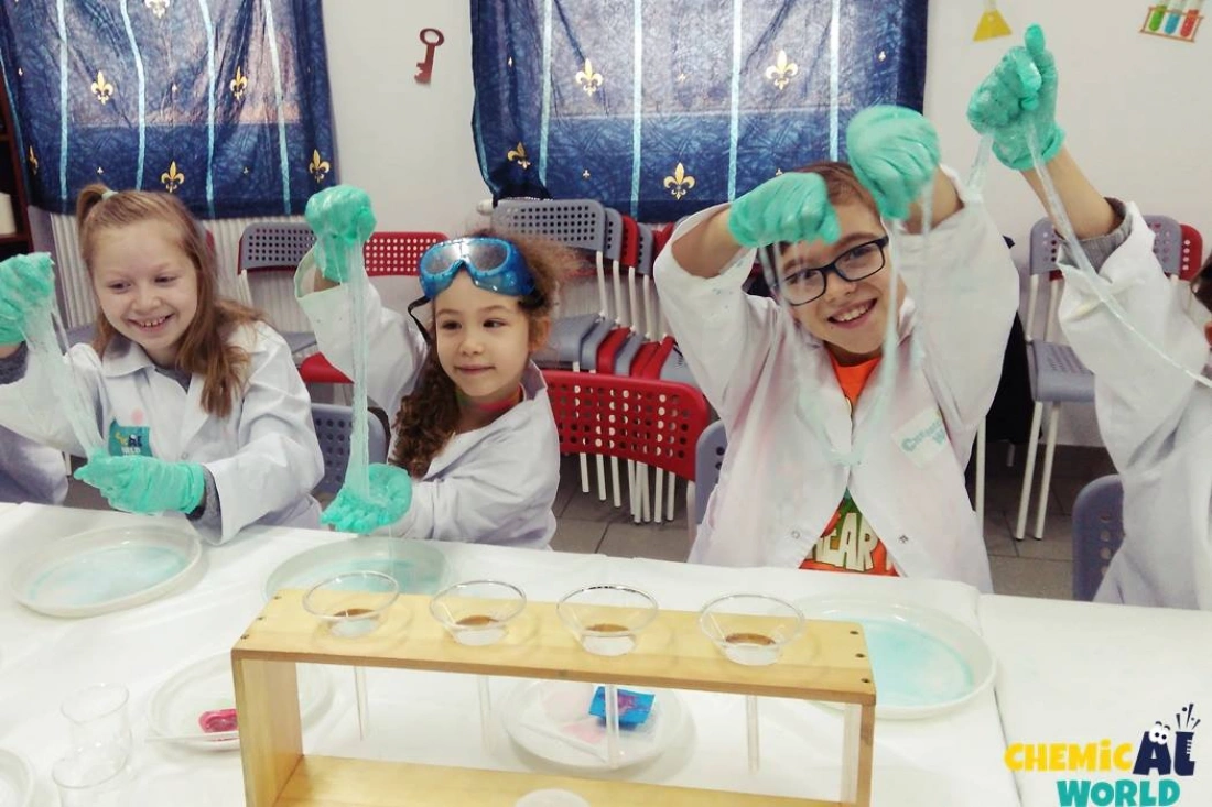 Dzieci w białych fartuchach laboratoryjnych bawią się slime'm w trakcie zajęć chemicznych.